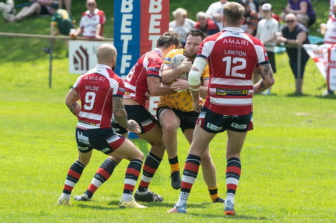 Cornwall's George Mitchell getting tackled by three Oldham players.